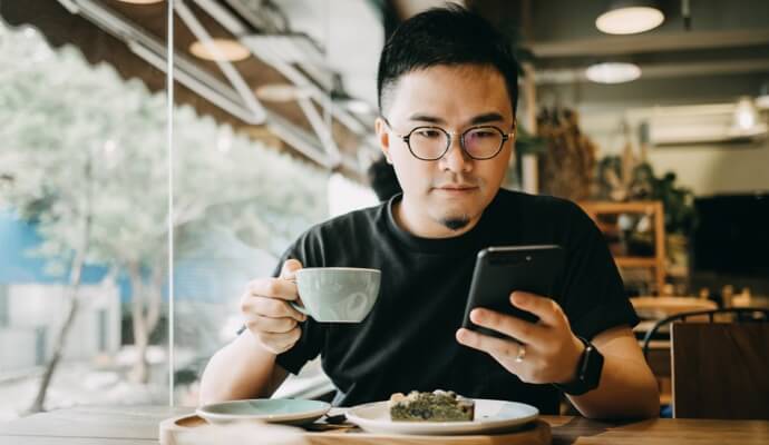 man die van zijn eten geniet en op mobiele telefoon kijkt waarop Norton 360 Standard wordt gestart.