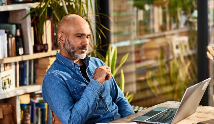 Man zit aan een bureau en kijkt naar een laptop