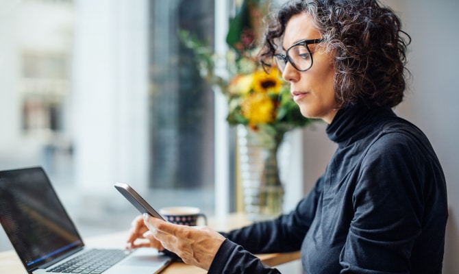 Vrouw die naar een mobiele telefoon kijkt voor een laptop